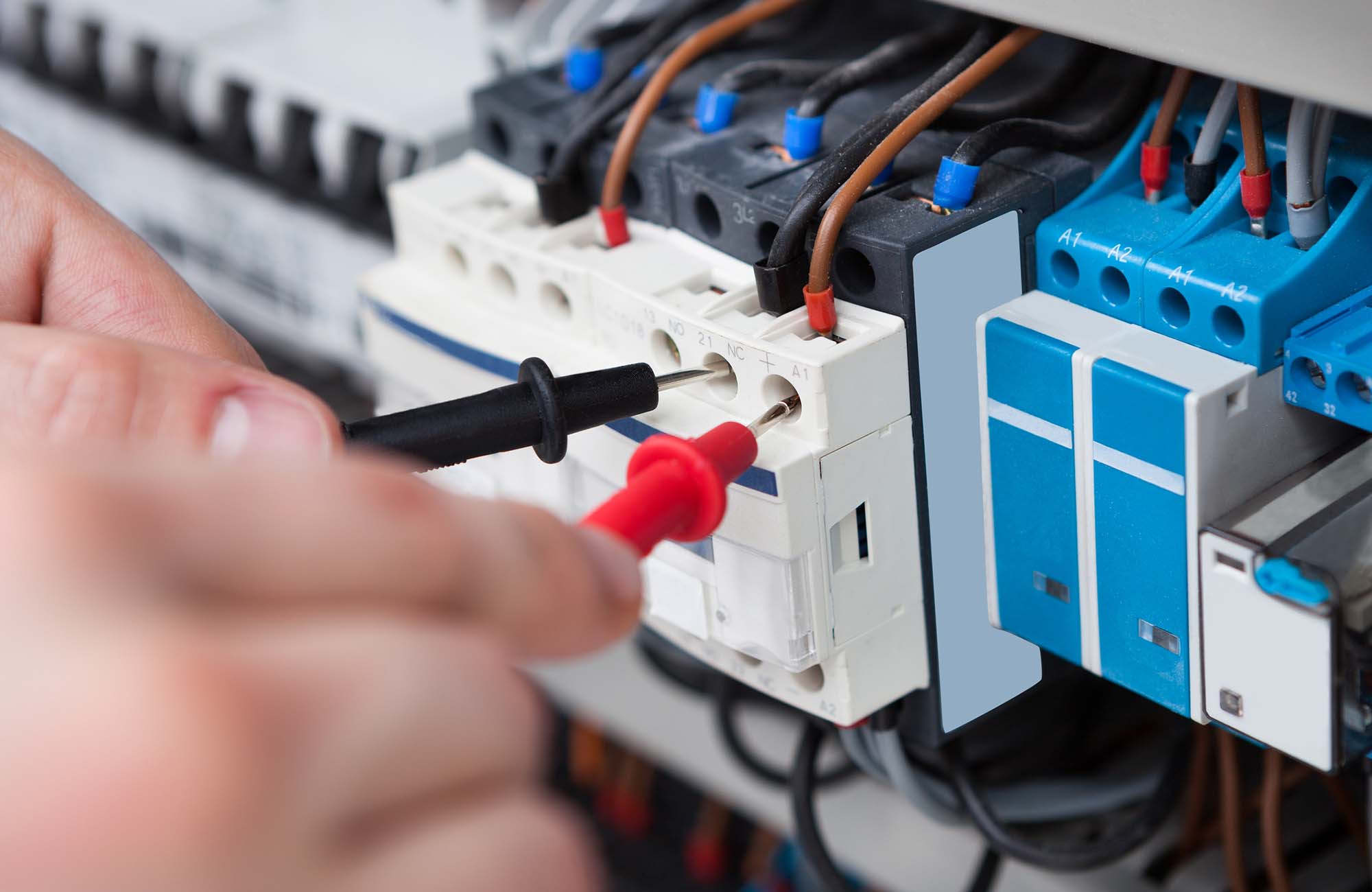 Closeup of male electrician examining fusebox with multimeter probe